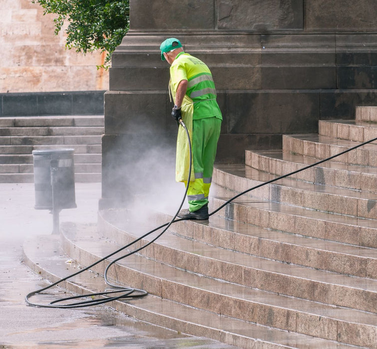 Worker pressure washing exterior stairs with heavy-duty washer