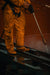 Worker in protective gear using a pressure washer on industrial equipment